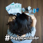Stressed woman looking at bills and credit cards on floor with headline "#PayDownDebt"