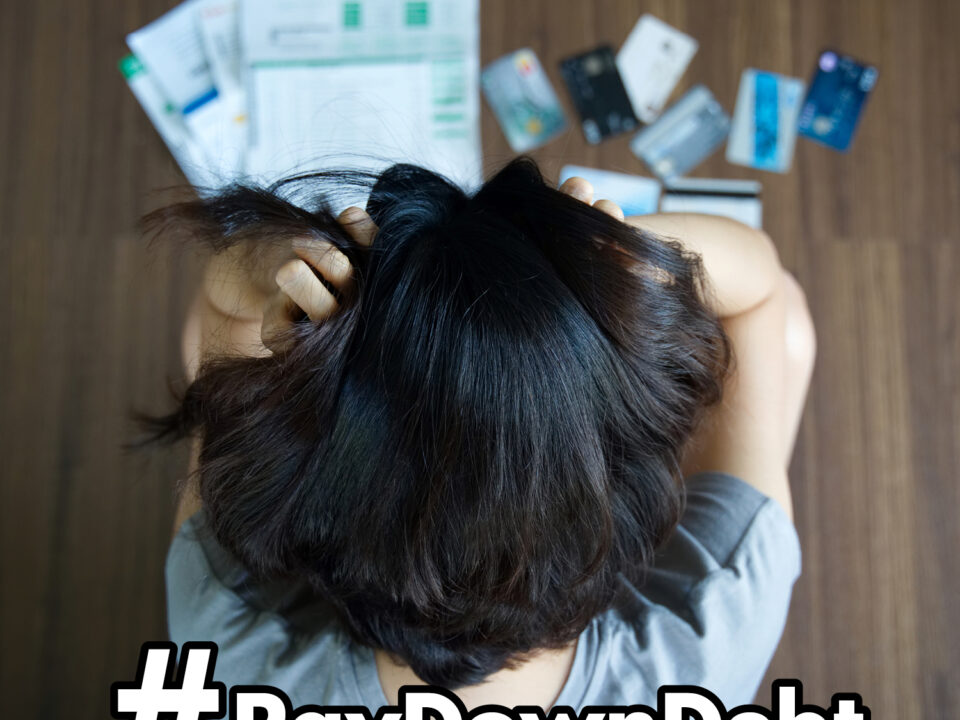 Stressed woman looking at bills and credit cards on floor with headline "#PayDownDebt"