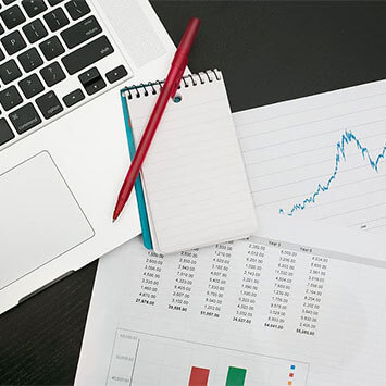 Pen, paper, laptop and printed charts resting on table.