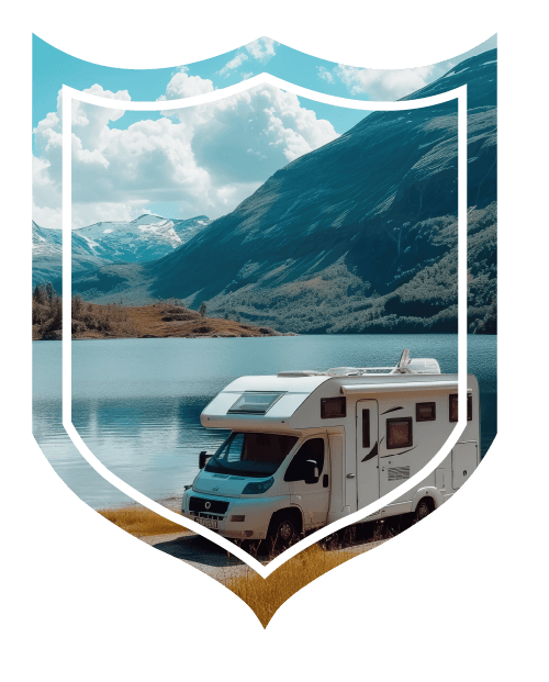 RV sitting in gravel lot next to blue water and mountainscape in background.