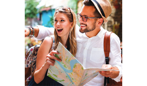 Couple standing close together holding map and pointing toward something in distance.