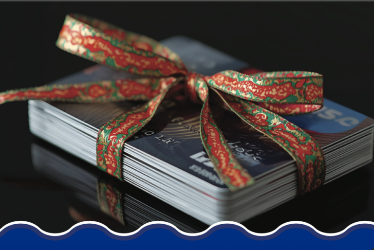 A stack of credit cards tied with a festive red and green ribbon, creating a gift-like appearance on a black reflective surface, suggesting holiday shopping.